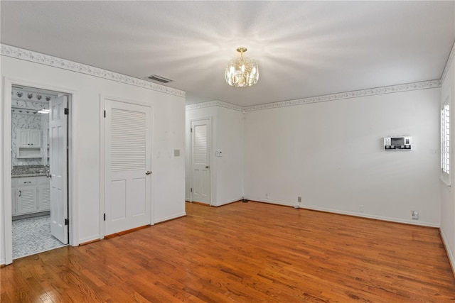 unfurnished bedroom featuring ensuite bath, a notable chandelier, and hardwood / wood-style flooring