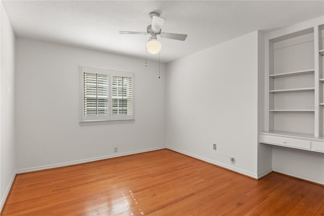 unfurnished room featuring a textured ceiling, built in desk, light hardwood / wood-style floors, and ceiling fan