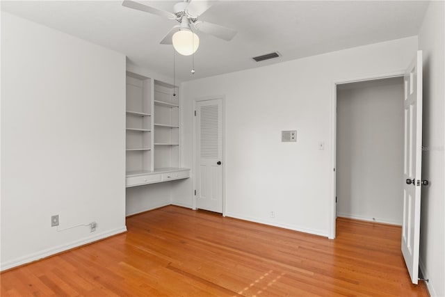 unfurnished bedroom featuring built in desk, light hardwood / wood-style floors, and ceiling fan