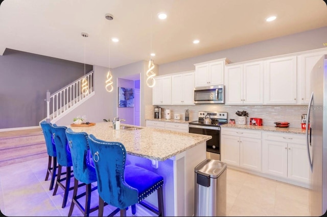 kitchen with white cabinetry, a center island with sink, stainless steel appliances, and decorative light fixtures