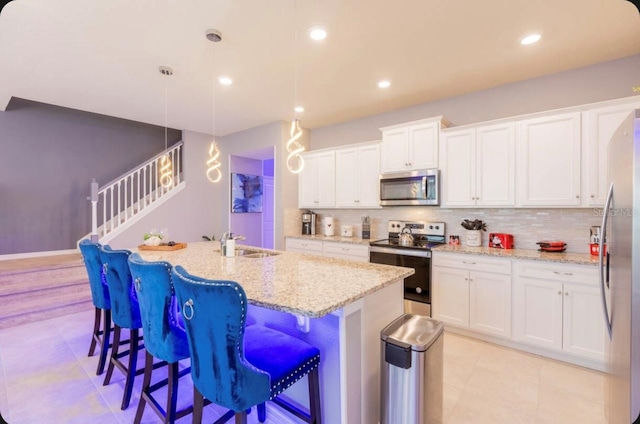 kitchen featuring white cabinetry, a kitchen island with sink, decorative light fixtures, and appliances with stainless steel finishes