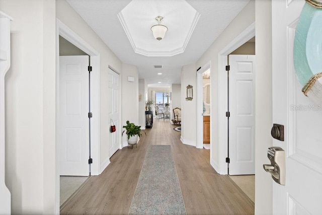 corridor with a raised ceiling and light hardwood / wood-style flooring