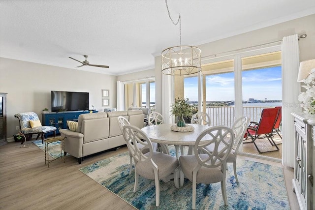 dining area featuring ornamental molding, a textured ceiling, ceiling fan with notable chandelier, a water view, and light hardwood / wood-style floors