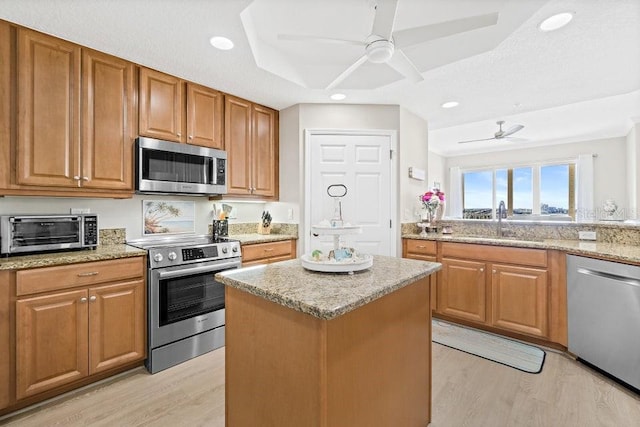 kitchen featuring light stone countertops, light wood-type flooring, stainless steel appliances, sink, and a kitchen island