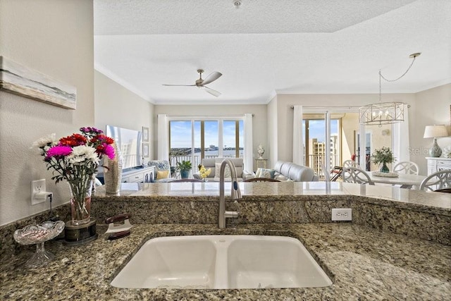 kitchen with ceiling fan with notable chandelier, a textured ceiling, dark stone countertops, and sink