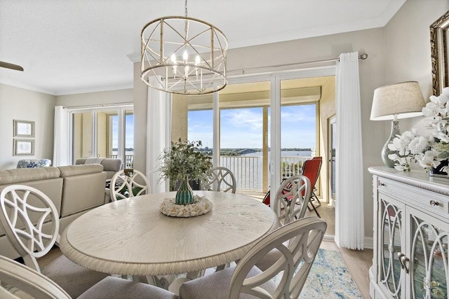 dining room featuring a notable chandelier, a water view, light wood-type flooring, and crown molding