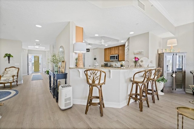 kitchen featuring a kitchen breakfast bar, ceiling fan, kitchen peninsula, and light hardwood / wood-style flooring