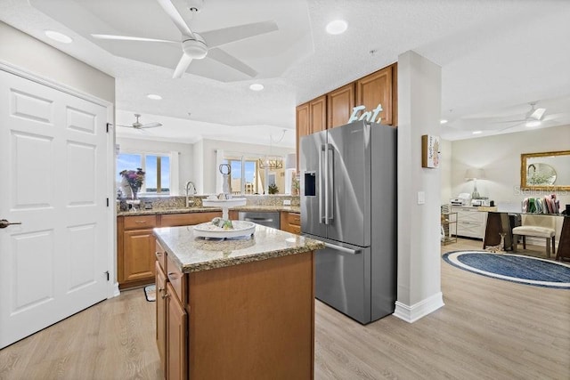 kitchen with sink, light wood-type flooring, a tray ceiling, a kitchen island, and stainless steel appliances