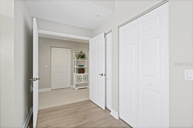 hall featuring light wood-type flooring and a textured ceiling