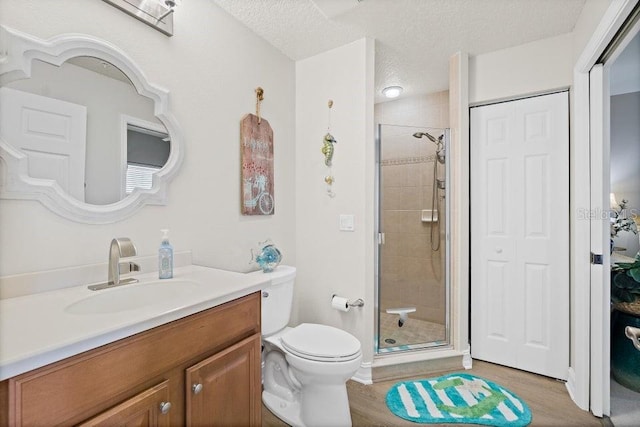 bathroom featuring wood-type flooring, a textured ceiling, toilet, a shower with door, and vanity