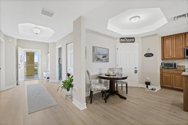 dining space featuring a textured ceiling, a tray ceiling, and light hardwood / wood-style flooring