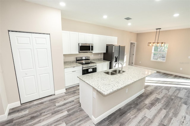 kitchen with hanging light fixtures, sink, stainless steel appliances, and a center island with sink