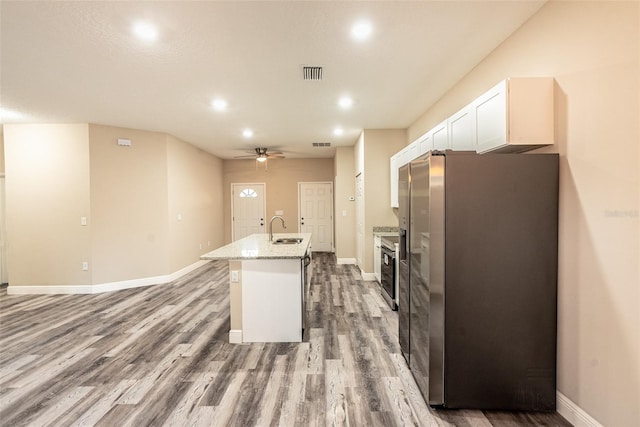 kitchen with stainless steel refrigerator, light stone counters, an island with sink, wood-type flooring, and white cabinets