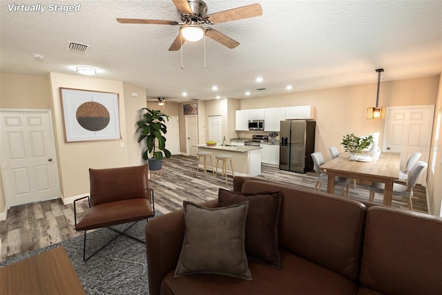 living room with a textured ceiling, light hardwood / wood-style floors, ceiling fan, and sink