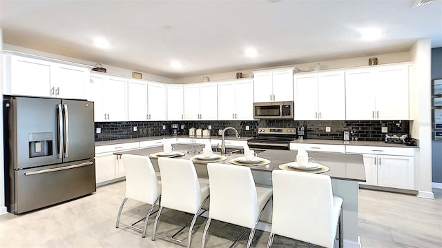 kitchen featuring decorative backsplash, an island with sink, white cabinets, and stainless steel appliances