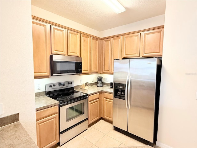 kitchen with light brown cabinetry, a textured ceiling, stainless steel appliances, and light tile patterned flooring