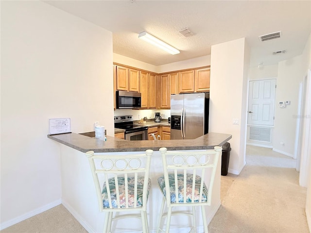 kitchen with kitchen peninsula, appliances with stainless steel finishes, a kitchen bar, a textured ceiling, and light colored carpet