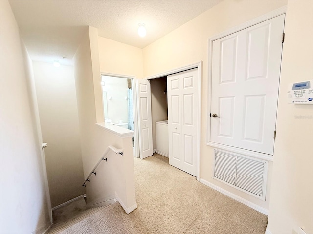 hall with light carpet and a textured ceiling