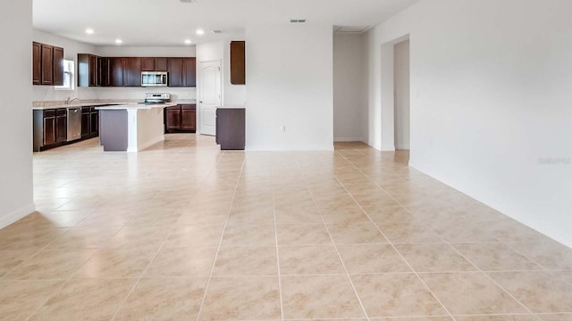 kitchen with dark brown cabinets, a kitchen island, light tile patterned flooring, and appliances with stainless steel finishes