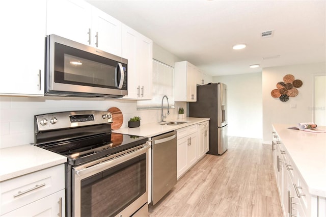 kitchen with light wood-type flooring, stainless steel appliances, white cabinetry, and backsplash