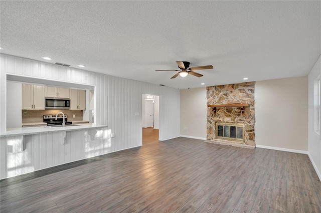 unfurnished living room featuring a stone fireplace, sink, ceiling fan, a textured ceiling, and dark hardwood / wood-style flooring