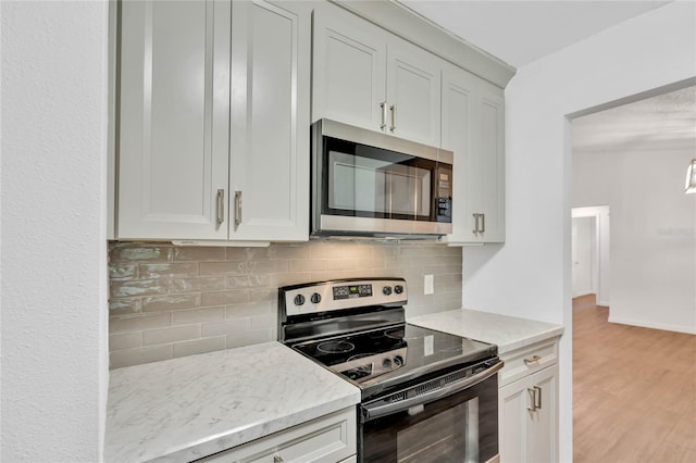 kitchen with tasteful backsplash, light stone counters, light wood-type flooring, and appliances with stainless steel finishes