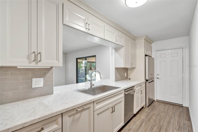 kitchen featuring light stone countertops, sink, stainless steel appliances, tasteful backsplash, and light wood-type flooring