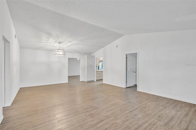 spare room with lofted ceiling, a textured ceiling, and light hardwood / wood-style flooring