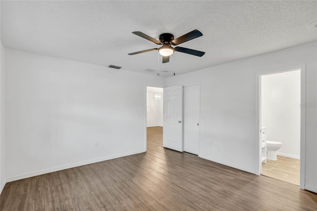 unfurnished bedroom with ensuite bath, ceiling fan, a textured ceiling, and hardwood / wood-style flooring