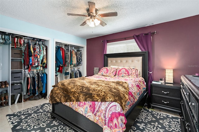 bedroom with a textured ceiling, two closets, ceiling fan, and light tile patterned flooring