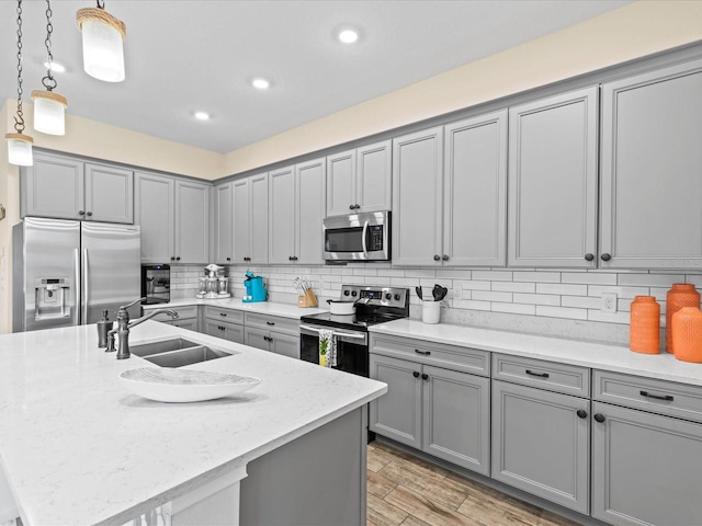 kitchen featuring a center island with sink, hanging light fixtures, sink, gray cabinets, and appliances with stainless steel finishes