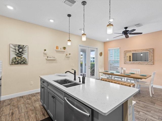 kitchen featuring a kitchen island with sink, sink, stainless steel dishwasher, and light wood-type flooring