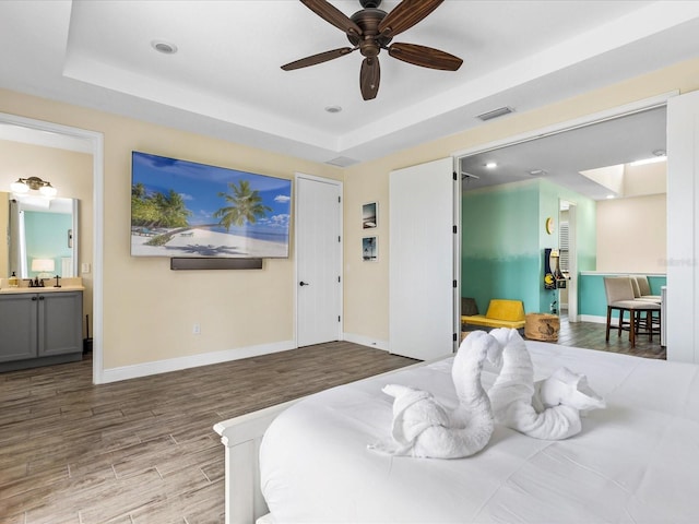 bedroom with connected bathroom, ceiling fan, sink, a raised ceiling, and light wood-type flooring