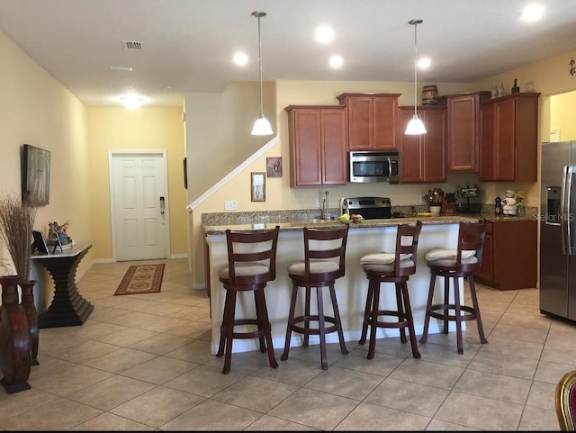 kitchen featuring stainless steel appliances, decorative light fixtures, stone countertops, an island with sink, and light tile patterned flooring