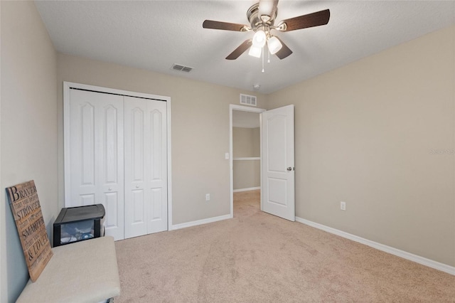 unfurnished bedroom featuring a textured ceiling, ceiling fan, light carpet, and a closet