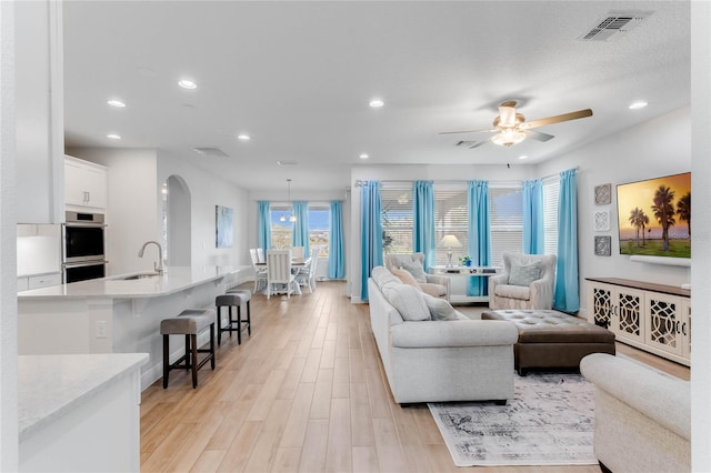 living room with ceiling fan, sink, and light wood-type flooring