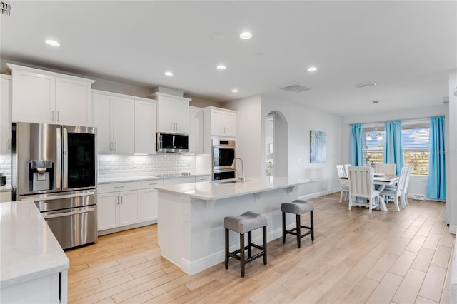 kitchen with appliances with stainless steel finishes, decorative light fixtures, a center island with sink, white cabinets, and light wood-type flooring