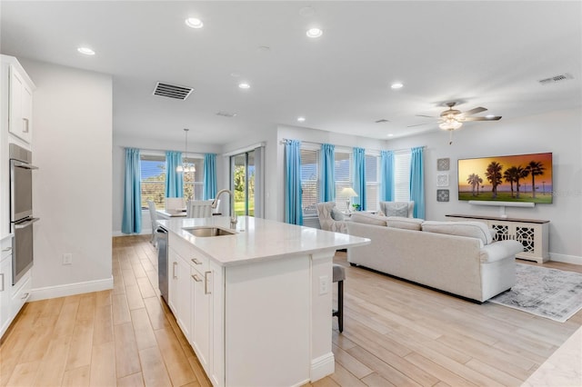 kitchen featuring ceiling fan with notable chandelier, sink, a center island with sink, light hardwood / wood-style flooring, and white cabinetry