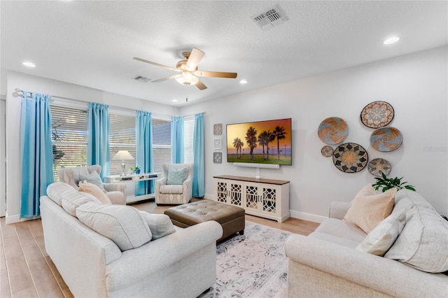 living room featuring a textured ceiling, light wood-type flooring, and ceiling fan