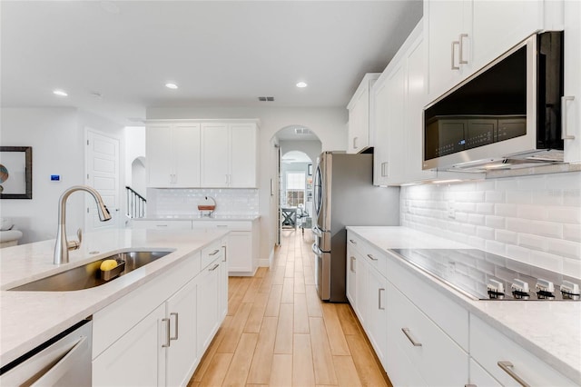 kitchen with white cabinets, sink, decorative backsplash, appliances with stainless steel finishes, and light hardwood / wood-style floors