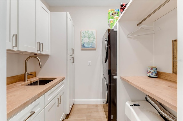 clothes washing area featuring sink, cabinets, stacked washer and dryer, and light hardwood / wood-style flooring