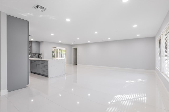 interior space featuring tasteful backsplash, gray cabinetry, light stone countertops, and light tile patterned floors