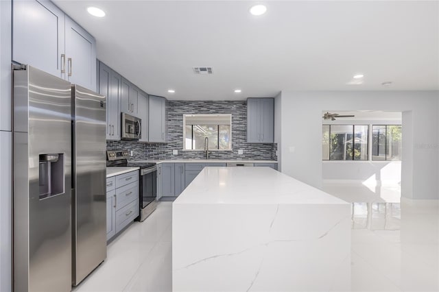 kitchen with a wealth of natural light, light stone countertops, a center island, and appliances with stainless steel finishes