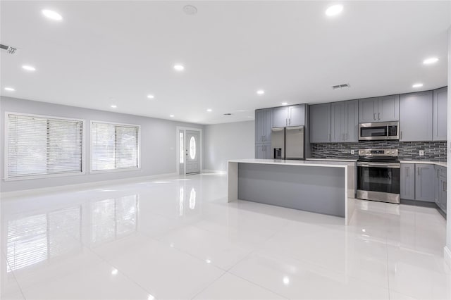 kitchen with gray cabinetry, a center island, decorative backsplash, light tile patterned floors, and appliances with stainless steel finishes