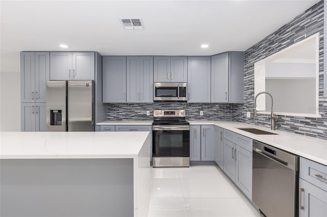 kitchen featuring light stone countertops, sink, backsplash, gray cabinets, and appliances with stainless steel finishes