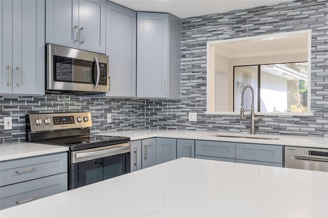 kitchen with gray cabinets, decorative backsplash, sink, and appliances with stainless steel finishes