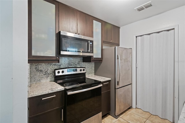 kitchen featuring backsplash, light stone countertops, light tile patterned floors, appliances with stainless steel finishes, and dark brown cabinetry