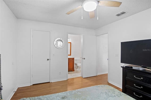 bedroom with ceiling fan, ensuite bath, a textured ceiling, and light hardwood / wood-style flooring