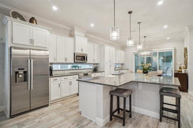 kitchen featuring white cabinetry, hanging light fixtures, stainless steel appliances, light hardwood / wood-style floors, and a kitchen island with sink