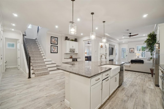 kitchen with pendant lighting, a kitchen island with sink, sink, light hardwood / wood-style flooring, and white cabinetry